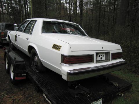 1991 Ford LTD Crown Victoria - A white sedan, possibly a police car, is loaded onto a trailer with a flat tire.