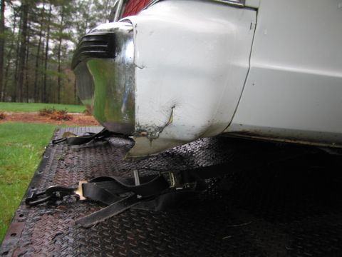 1991 Ford LTD Crown Victoria - The rear of a white vehicle shows significant damage to the bumper and quarter panel, with straps securing it to a trailer.