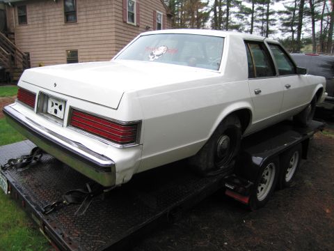 1991 Ford LTD Crown Victoria - White sedan being transported on a trailer, rear view showing taillights and chrome bumper.