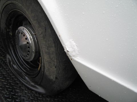 1991 Ford LTD Crown Victoria - Close-up of a white car's fender showing rust and a flat tire.