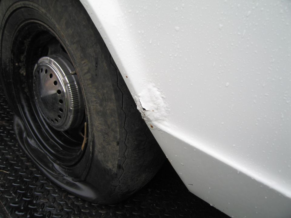 White car fender with rust patch and flat tire