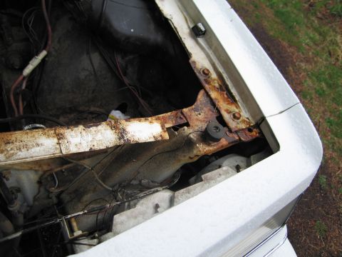 1991 Ford LTD Crown Victoria - Close-up view of a white car's engine bay, highlighting the corroded hood latch area and exposed wiring.