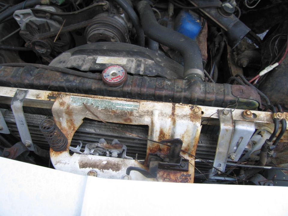 Engine bay showing radiator, fan shroud, and hoses. Radiator cap has text