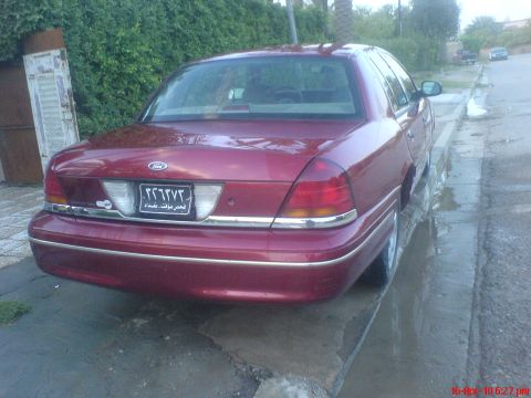 1998 Ford Crown Victoria - Rear view of a red 1998 Ford Crown Victoria parked on a wet street.