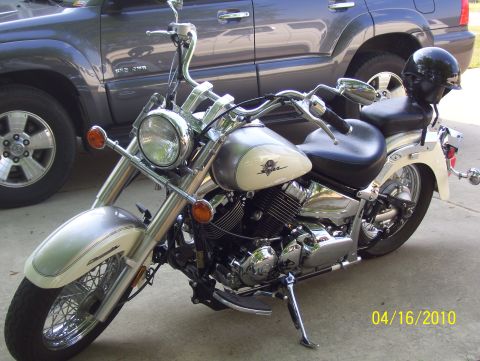 1978 Ford Bronco - A cream and chrome motorcycle is parked in front of a dark SUV, with a helmet on the passenger seat.