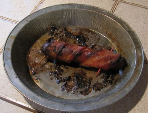 1990 Ford Bronco - A close-up view of a meat item wrapped in bacon and secured with toothpicks, resting in a pie tin.