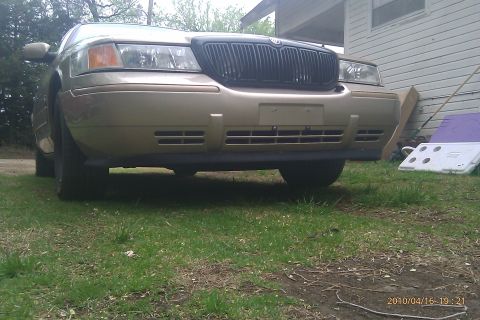 2000 Mercury Grand Marquis - The front end of a gold Mercury Grand Marquis is shown parked on grass in front of a building.