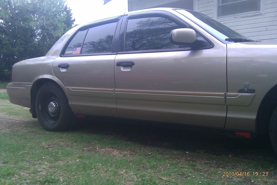 Tan sedan parked on grass, side view. American flag sticker on rear window