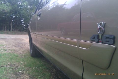 2000 Mercury Grand Marquis - Side view of a gold sedan, showing a 4.6 badge and a reflection of a red truck in the door.