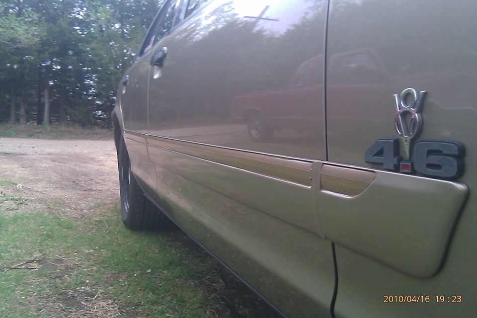 Gold sedan side view with 4.6 badge. Red truck reflected in door