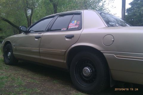 2000 Mercury Grand Marquis - Side profile of a gold 2000 Mercury Grand Marquis, aftermarket stickers on the rear passenger window.