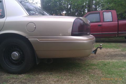 2000 Mercury Grand Marquis - A tan sedan is parked next to a red pickup truck, showing the rear passenger side of the sedan.