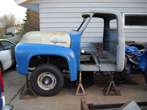 1954 Ford F-100 - A partially disassembled Ford truck sits on jack stands in front of a garage.