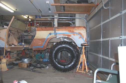 Rusted vehicle body on jack stands with a large tire, in a garage