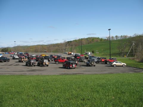 1985 Ford Bronco - A large group of Jeeps are parked in an outdoor lot under a clear blue sky.