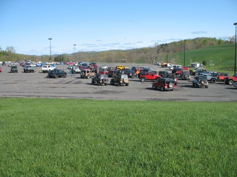 1985 Ford Bronco - A large gathering of SUVs, predominantly Jeeps, are parked in an outdoor lot on a sunny day.