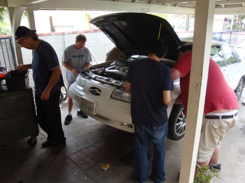 1995 Ford Taurus - Mechanics work on a white 1995 Ford Taurus with its hood open.