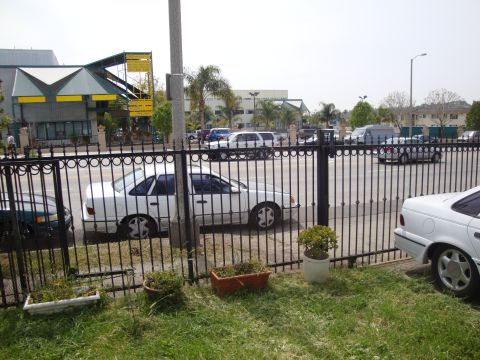 1995 Ford Taurus - A white sedan is parked behind a decorative black metal fence, with other vehicles and buildings visible in the distance.