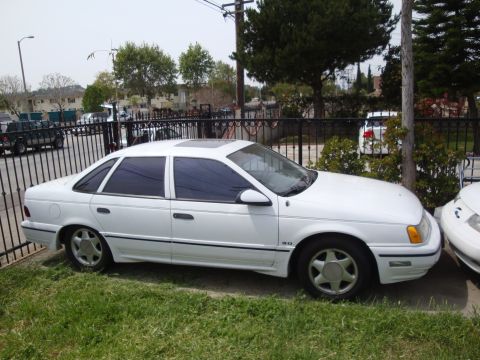 1995 Ford Taurus - A white 1995 Ford Taurus sedan is parked on a grassy area next to a fence.