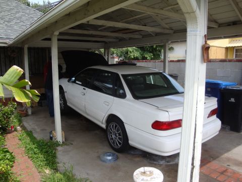 1995 Ford Taurus - White 1995 Ford Taurus sedan parked under a carport with hood open, showing its rear quarter panel and trunk.