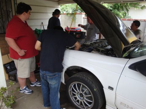 1995 Ford Taurus - Mechanics work on the engine of a white 1995 Ford Taurus with its hood open.