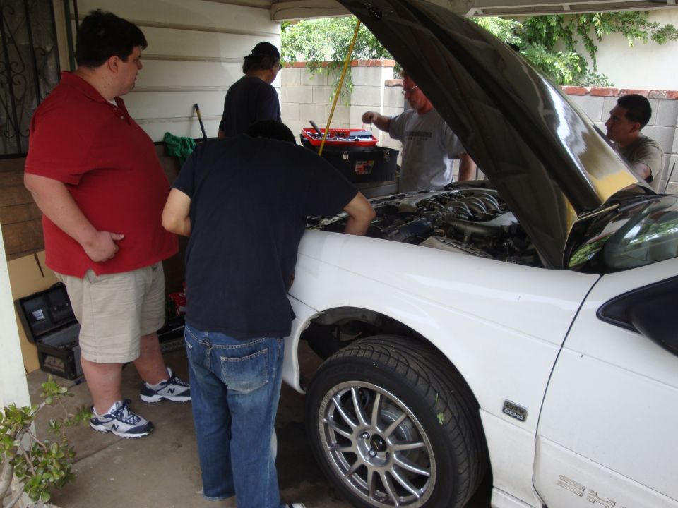 White 1995 Ford Taurus with hood open, people gathered around the engine
