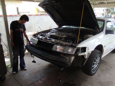 1995 Ford Taurus - Front end of a 1995 Ford Taurus undergoing maintenance, hood is up and bumper is detached.