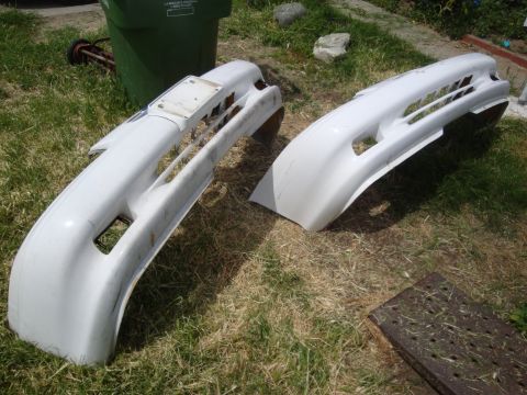 1995 Ford Taurus - Two white car bumpers are displayed on a grassy area next to a green trash bin.