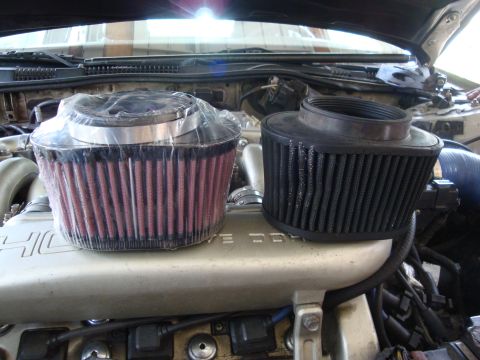 1995 Ford Taurus - Comparison of a new red air filter and a used black air filter on top of an engine.