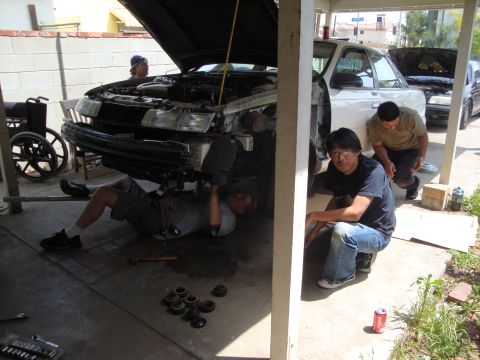 1995 Ford Taurus - Mechanics are working on the front of a car, with another vehicle in the background.