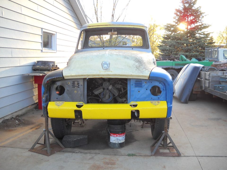 Front view of a 1953 Ford F-100 truck on jack stands, engine exposed, with yellow bumper