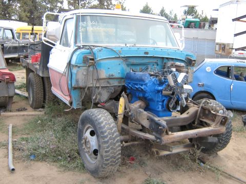 1972 Ford F-250 - A disassembled truck with a bright blue engine sits in a junkyard next to other vehicles.