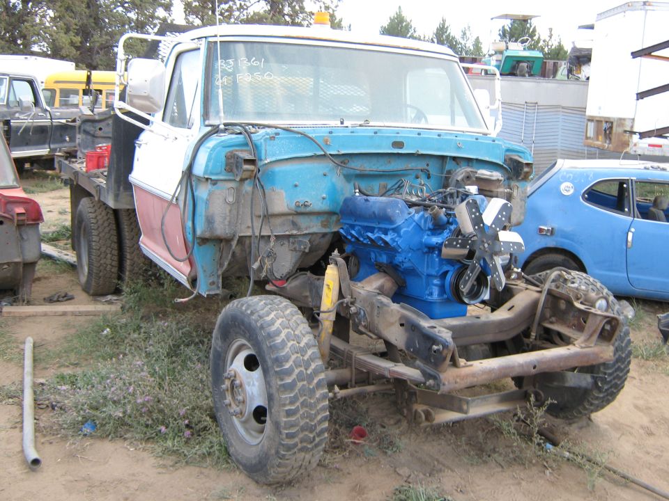 Truck chassis, blue engine, white cab, red fender, dual rear wheels, in junkyard