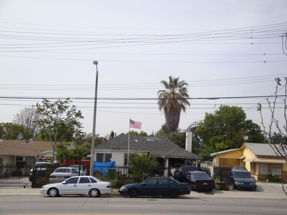 Street view of houses and several parked cars under a cloudy sky