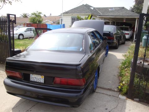 1995 Ford Taurus - A black sedan with bright blue wheels is parked in a driveway, with its hood open, alongside two other vehicles.