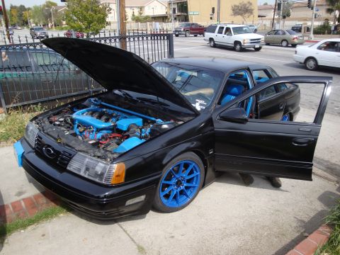 1995 Ford Taurus - Black 1995 Ford Taurus wagon with hood and driver door open, revealing blue engine parts and bright blue wheels.