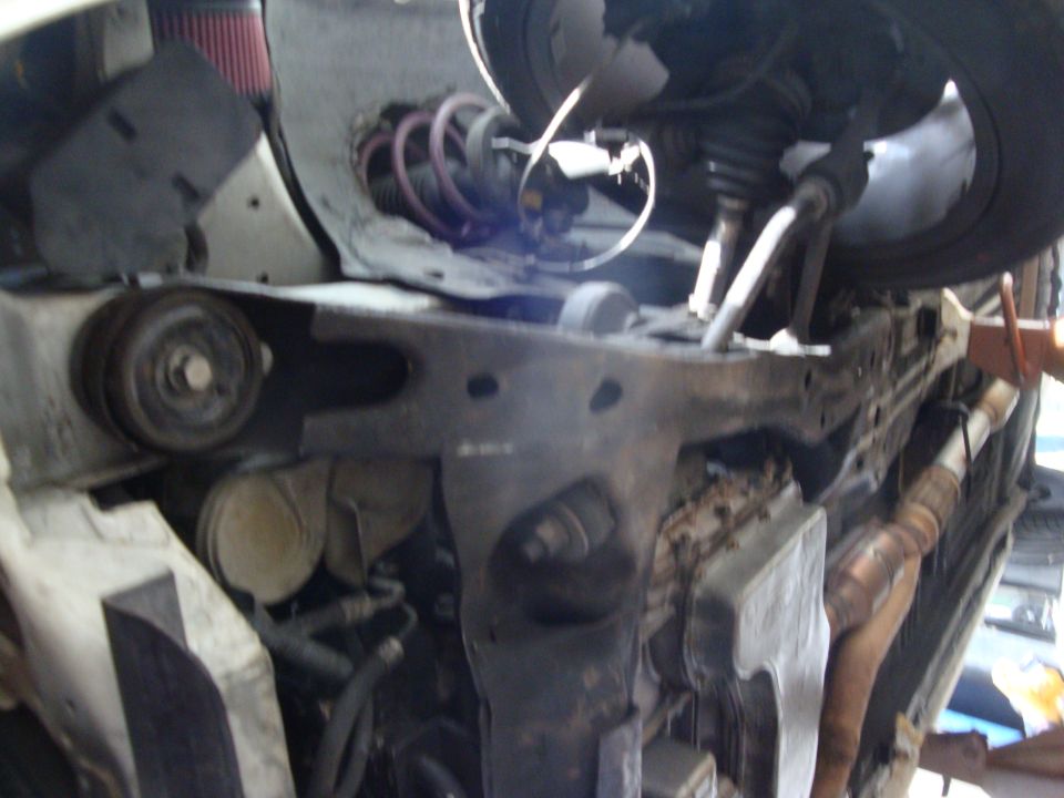 Underside view of car's engine bay showing suspension, pulley, and exhaust components