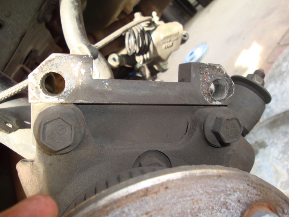 Close-up of a dusty brake caliper bracket with bolts and part of a rotor visible
