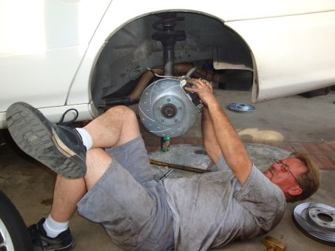 1995 Ford Taurus - A man performs maintenance on a vehicle's braking system, lying on the ground next to the car.