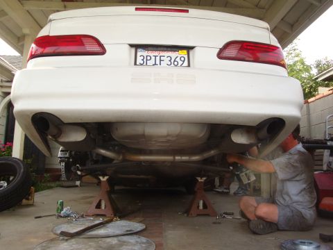 1995 Ford Taurus - A person works on the underside of a white sedan, which is elevated on jack stands.