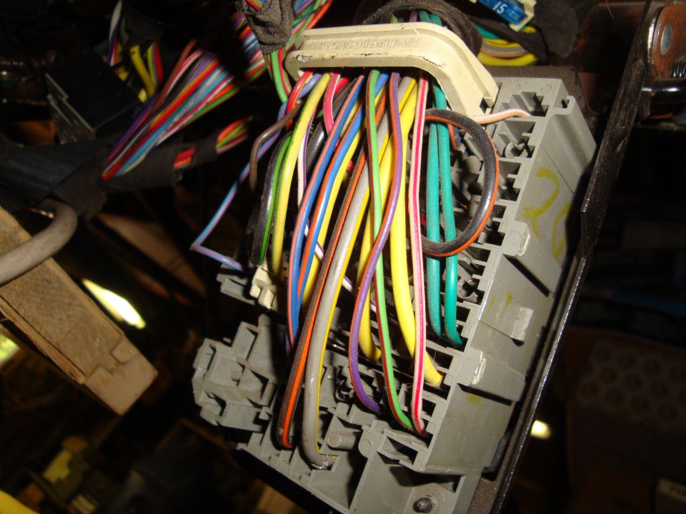 Close-up of a bundle of colorful wires connected to a gray plastic electrical connector in a vehicle