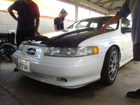 1995 Ford Taurus - Front view of a white 1995 Ford Taurus with a black hood and aftermarket wheels.