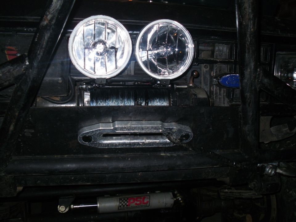 Off-road vehicle front end with winch, two round headlights, and a metal tow hook