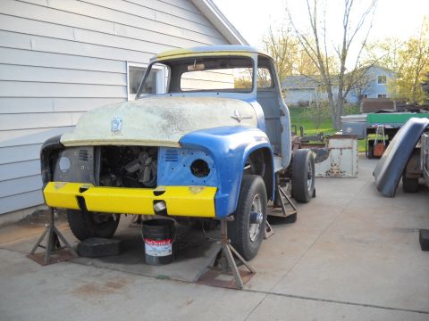 1954 Ford F-100 - Ford truck chassis undergoing restoration, front end visible with blue fenders and yellow bumper.