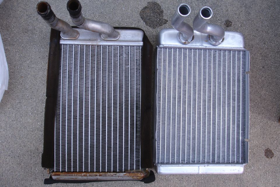 Old rusty heater core beside a new replacement heater core on concrete
