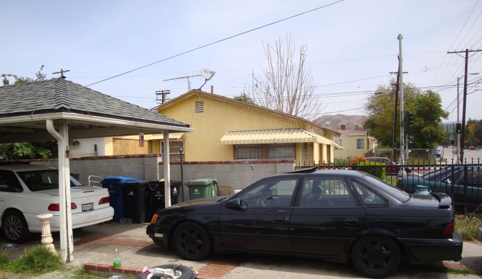 Black 1995 Ford Taurus sedan parked next to a white car under a carport