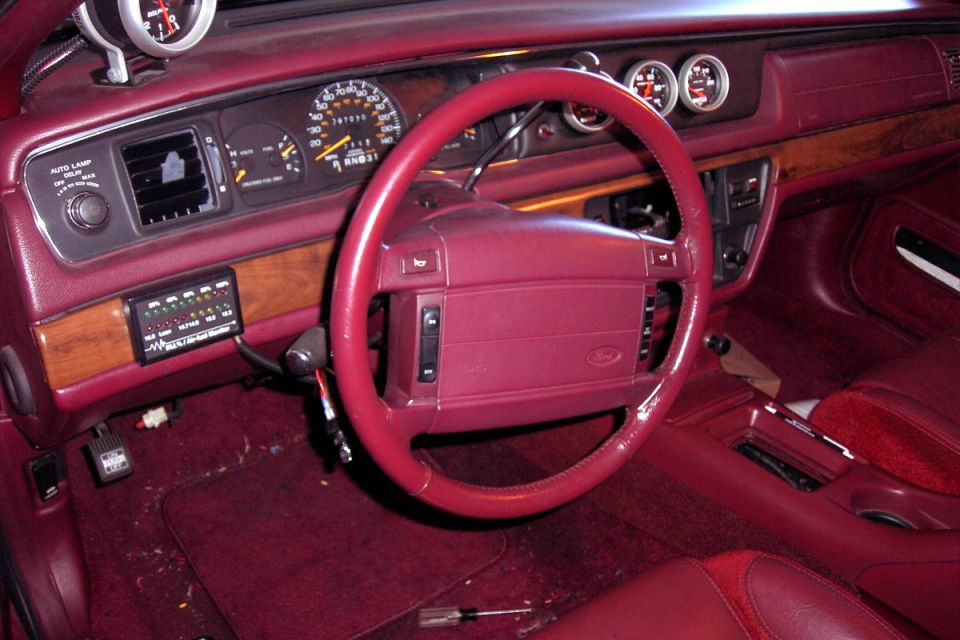 Burgundy Ford sedan interior with red steering wheel, woodgrain dash and added gauges