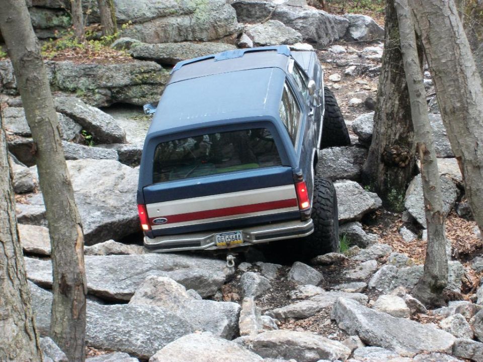 Blue SUV with red and white stripe on rear, navigating a rocky trail