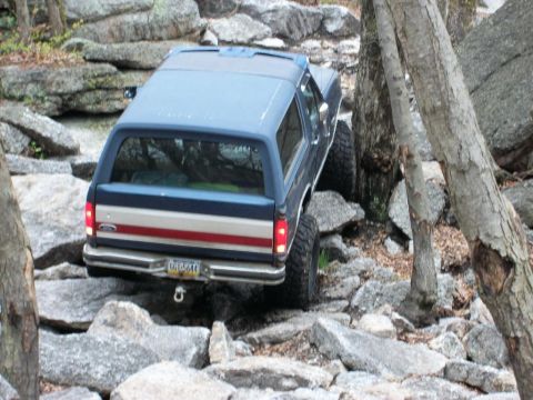 1986 Ford Bronco - This SUV, likely a 1987 model, is shown off-roading on a challenging rocky path.