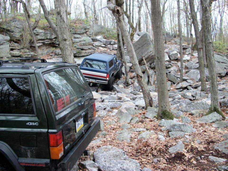 Blue 1987 Ford Bronco with red and white side stripes navigating a rocky trail